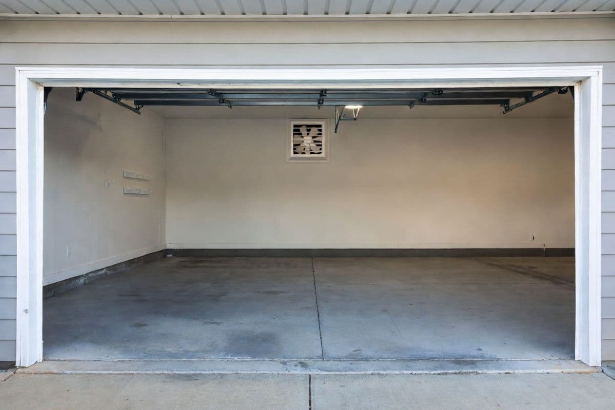 Residential garage interior with open garage door and wall-mounted exhaust fan visible on the rear wall showing active cross-ventilation