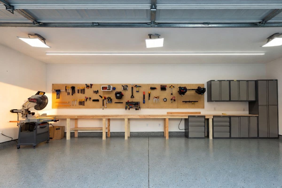 Organized garage workshop with epoxy floor, LED lighting, pegboard tool wall, workbench, and steel cabinet storage
