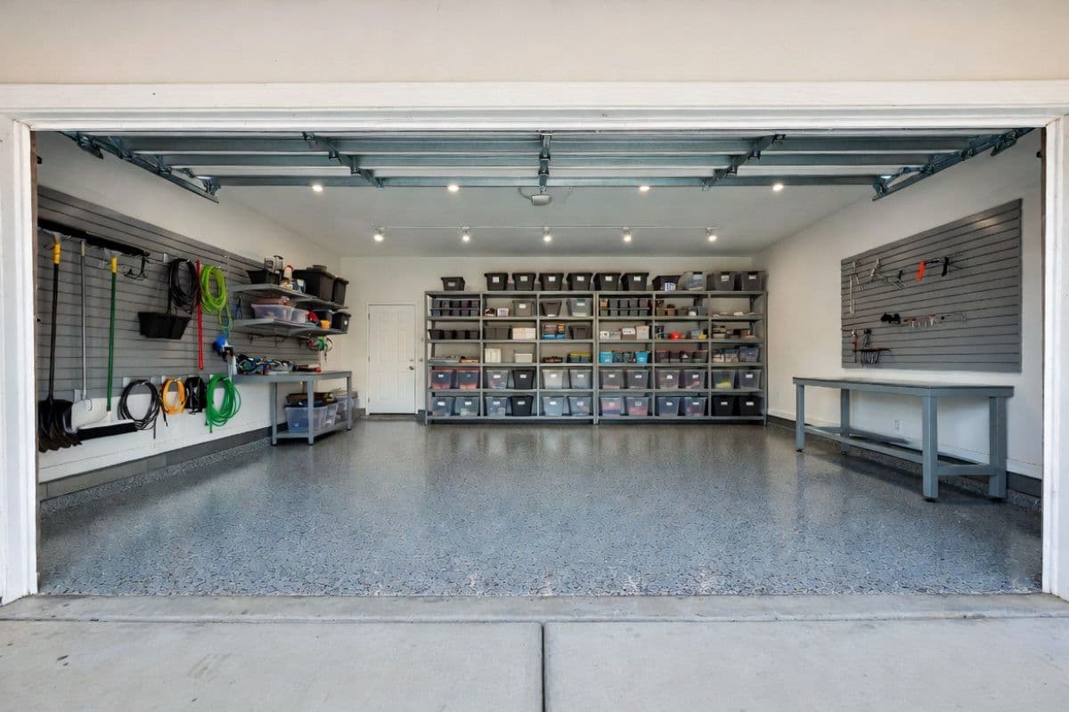 Interior of a well-organized two-car garage with wall-mounted storage systems, LED shop lighting, coated floor, workbench, and rear shelving.